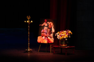 Stage memorial scene with a portrait on an easel beside a bouquet of flowers and lit candles in a candelabrum, soft warm lighting.